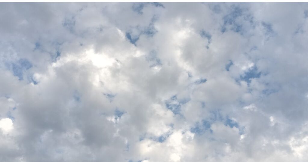 丸い綿状の灰色と白色の雲の多い空。　雲のすき間に青空が少しだけ見えている。