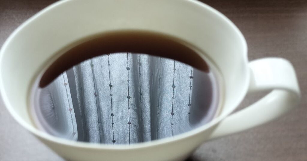 白いコーヒーカップの中のコーヒーに映るレースのカーテンと明るい陽射し