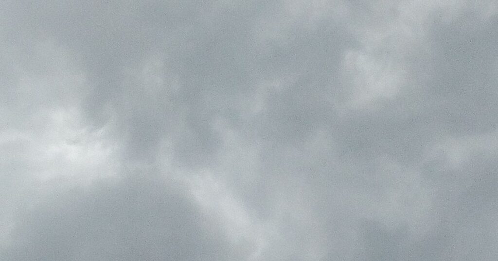 薄曇りの空。グレーの雲のすき間に少し明るい白い雲。